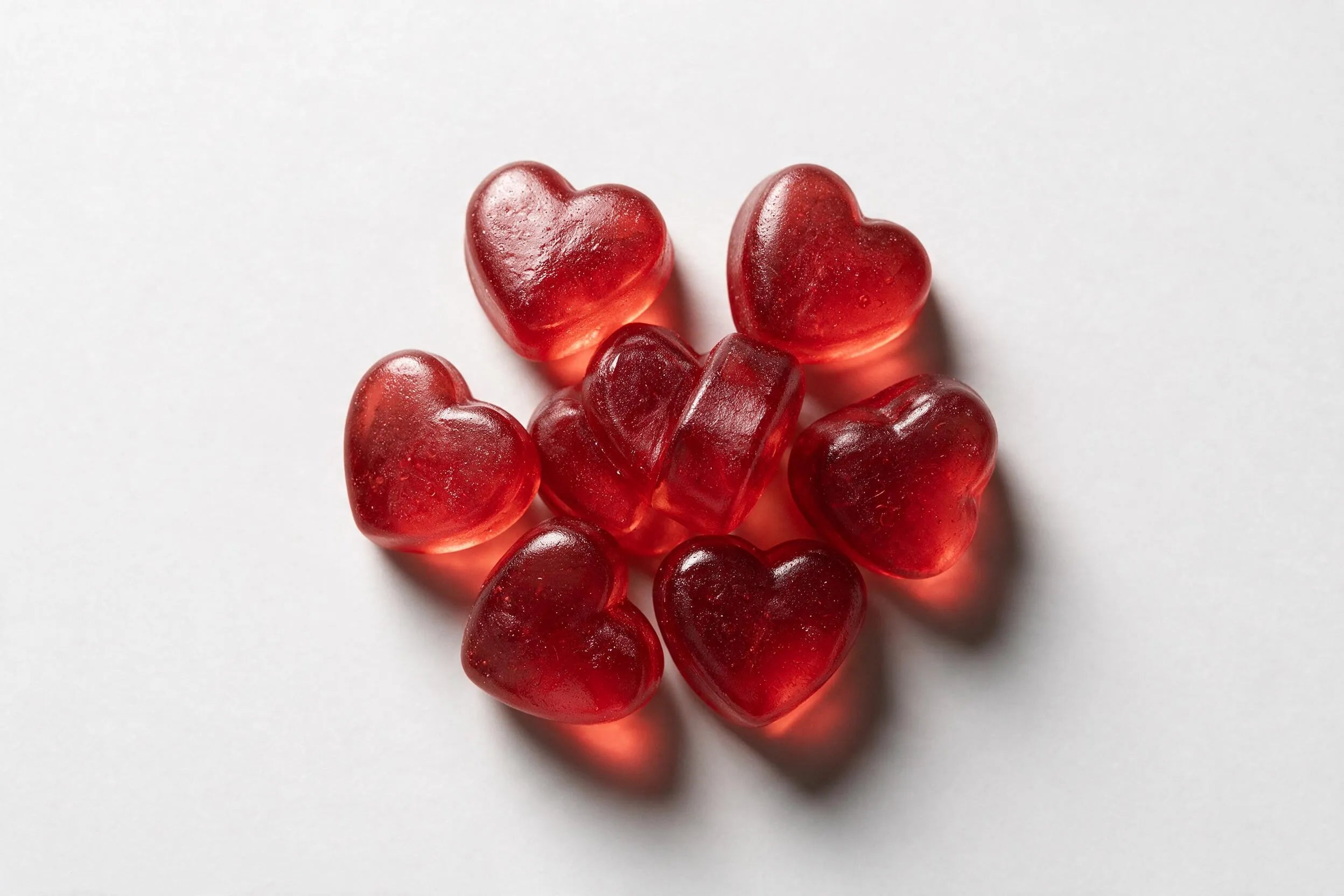 A loose pile of red heart-shaped gummies on a pale surface